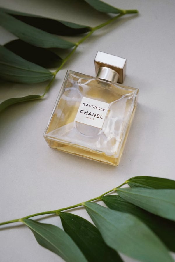 Gabrielle Essence perfume
         bottle laying flat on a table with 
         green leaves laying beside it in opposite direction